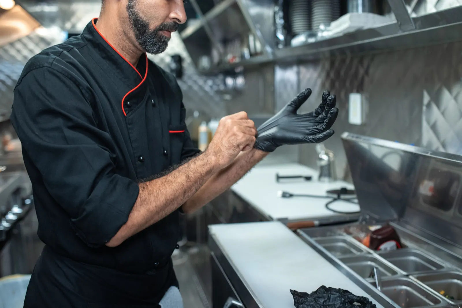 A chef pulling on black gloves in a steel kitchen