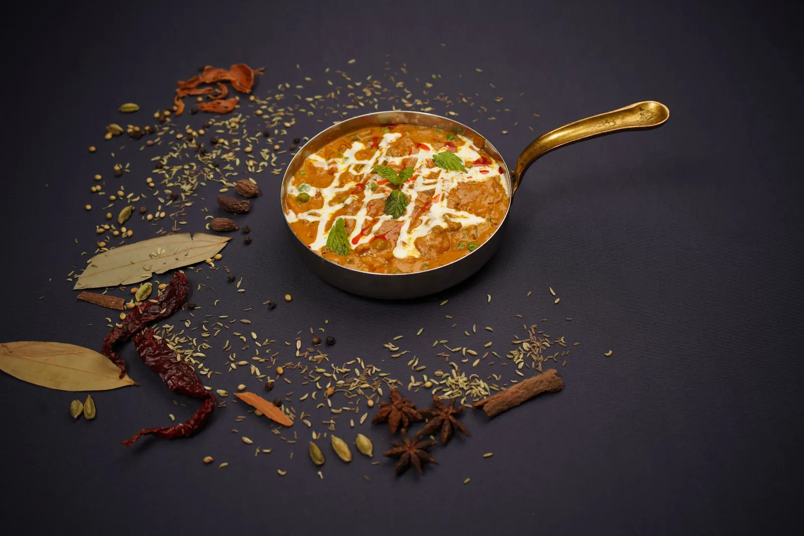 Curry in a bronze pan surrounded by whole spices